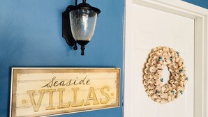 Un mur bleu avec une enseigne indiquant « VILLAS EN BORD DE MER » et une guirlande décorative sur une porte blanche.