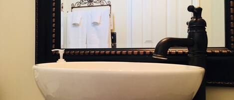 A white ceramic sink with a black faucet, a mirror with a decorative frame, and a towel rack with white towels.