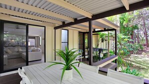 Ein Terrassenbereich im Freien mit Tisch und Stühlen, umgeben von Glastüren zu einem Wohnzimmer.