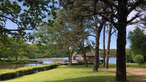Una propiedad junto al lago con un puente de madera, un césped y una casa con balcón con vistas al agua.