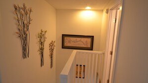 Un pasillo con barandilla blanca, un mapa enmarcado en la pared y ramas decorativas.