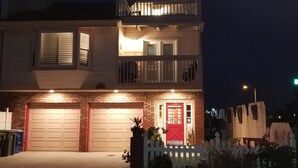 A two-story residential building with a red front door, a balcony on the upper floor, and a garage with two doors.