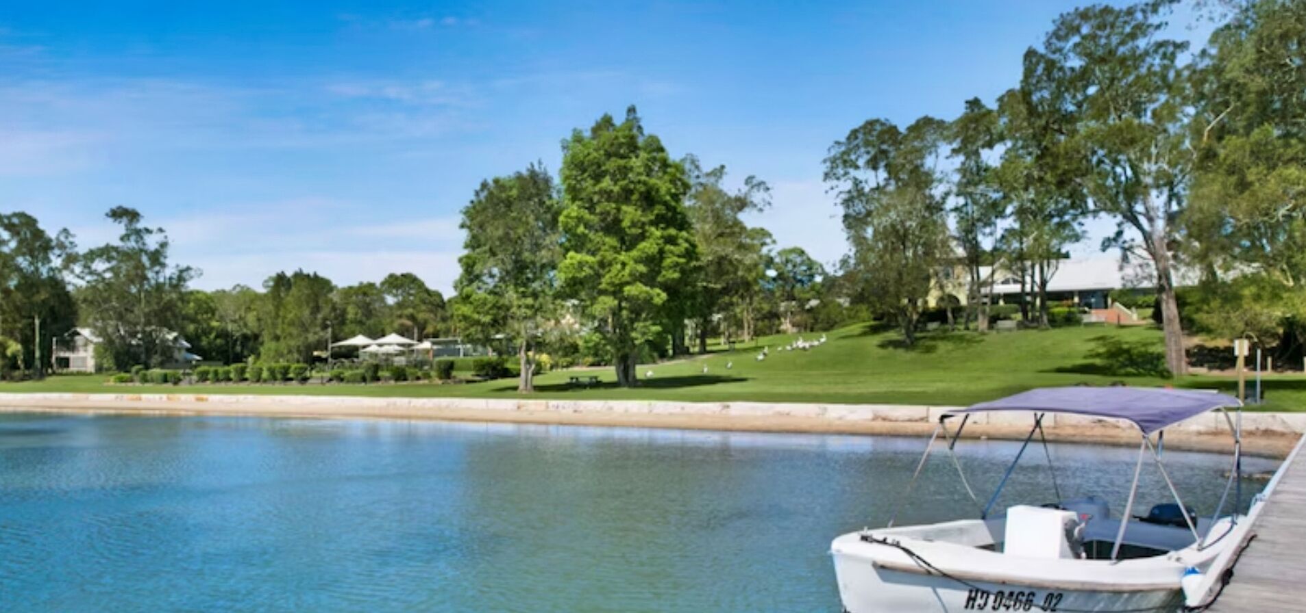A boat docked at a calm water body with a grassy area and trees in the background.
