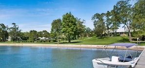A boat docked at a calm water body with a grassy area and trees in the background.