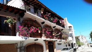 A building with a white facade, multiple balconies with hanging flower pots, and a car parked in front. - Casa Alexandra. Puerto Vallarta Traditional Comfort. (Puerto Vallarta)