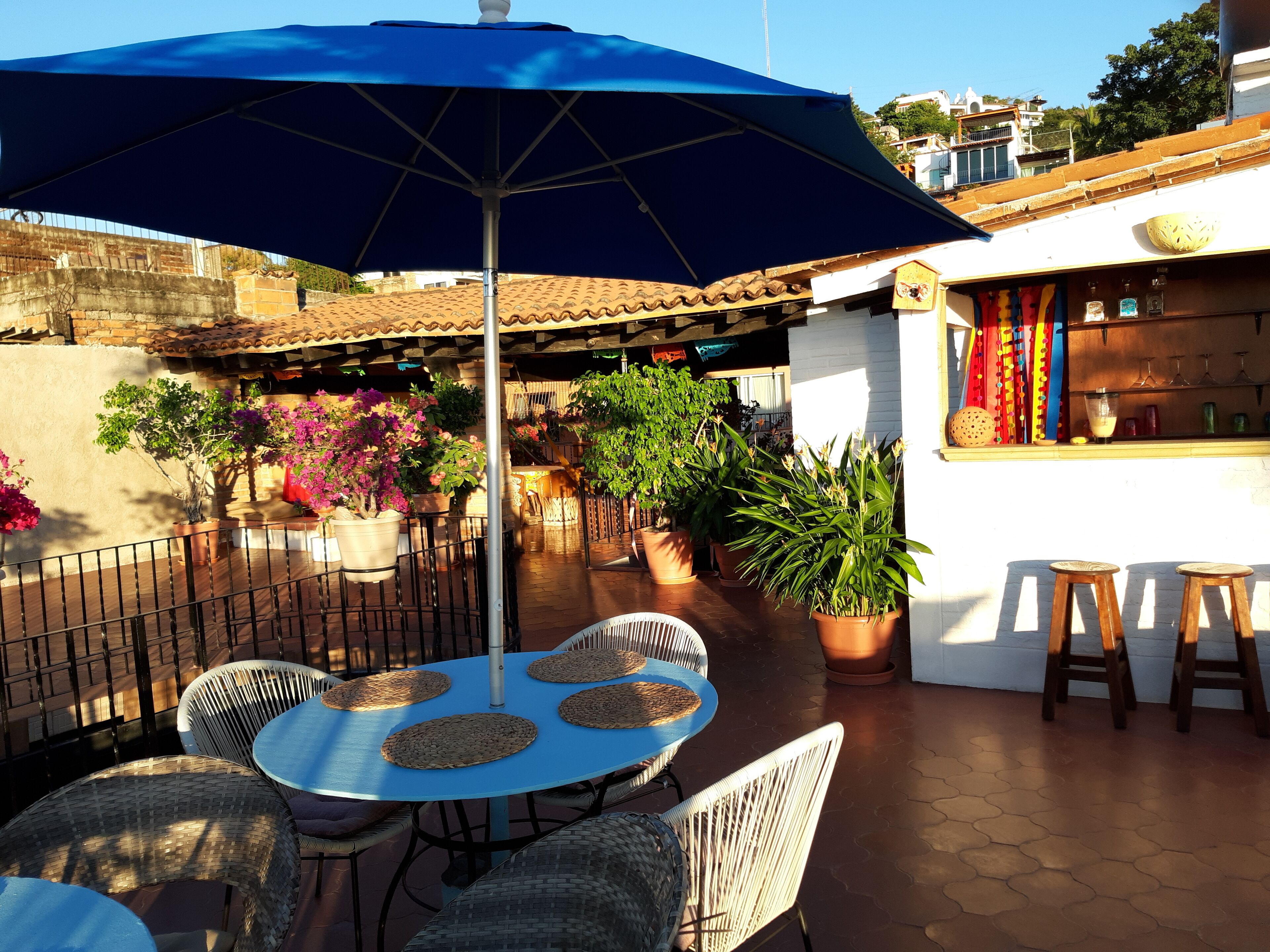 Une terrasse extérieure avec un parasol bleu, des chaises en osier et des plantes en pot.