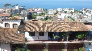 A multi-story building with a tiled roof, balconies with potted plants, and a view of the sea. - Casa Alexandra. Puerto Vallarta Traditional Comfort. (Puerto Vallarta)