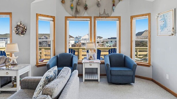 A living room with a view of houses through large windows, a starfish decoration, and a ceiling with hanging ornaments. - Blue Heron | 955 ft from the Beach | Private Pool, Hot Tub | Nags Head (Nags Head)