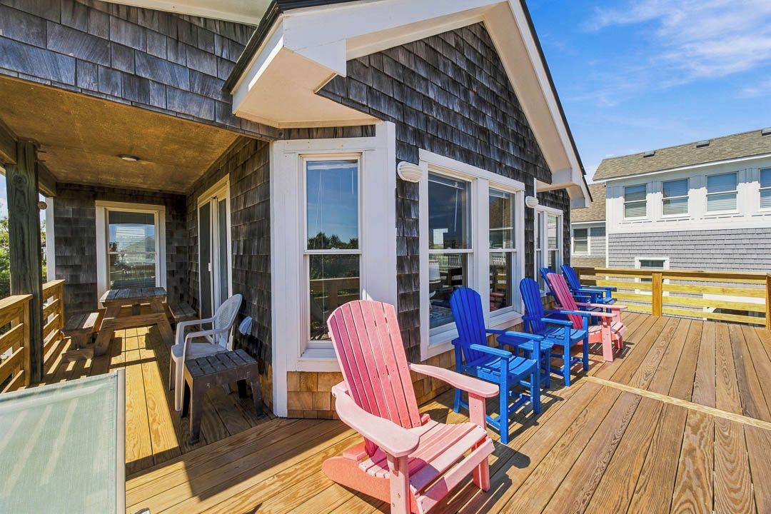 Una terraza techada con sillas Adirondack y una mesa de madera, con vistas a un barrio residencial.
