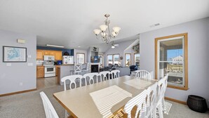 A spacious kitchen with modern appliances, a dining area with a large table and chairs, and a view through a window. - Blue Heron | 955 ft from the Beach | Private Pool, Hot Tub | Nags Head (Nags Head)