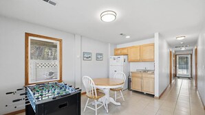 Uma cozinha com mesa de futebol, mesa de jantar com cadeiras, armários de madeira e uma geladeira.