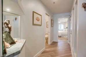 A hallway with a marble countertop, framed artwork, and a bed in the distance.