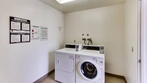 A laundry room with two washing machines and dryers, a ceiling light, and informational signs on the wall.