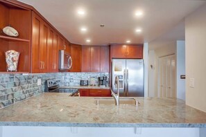 A kitchen with wooden cabinets, a stainless steel refrigerator, a granite countertop, and a built-in oven.