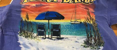 A blue t-shirt with a beach scene, featuring two chairs labeled "FLORA-BAMA" and the text "On the Beautiful Gulf of Mexico."