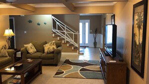 A living room with a sofa, coffee table, TV stand, and a staircase leading to another room. - Perdido Key/Pensacola Pass sleeps 14 (Pensacola)