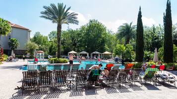 A poolside area with lounge chairs and umbrellas, surrounded by palm trees and a building in the background.