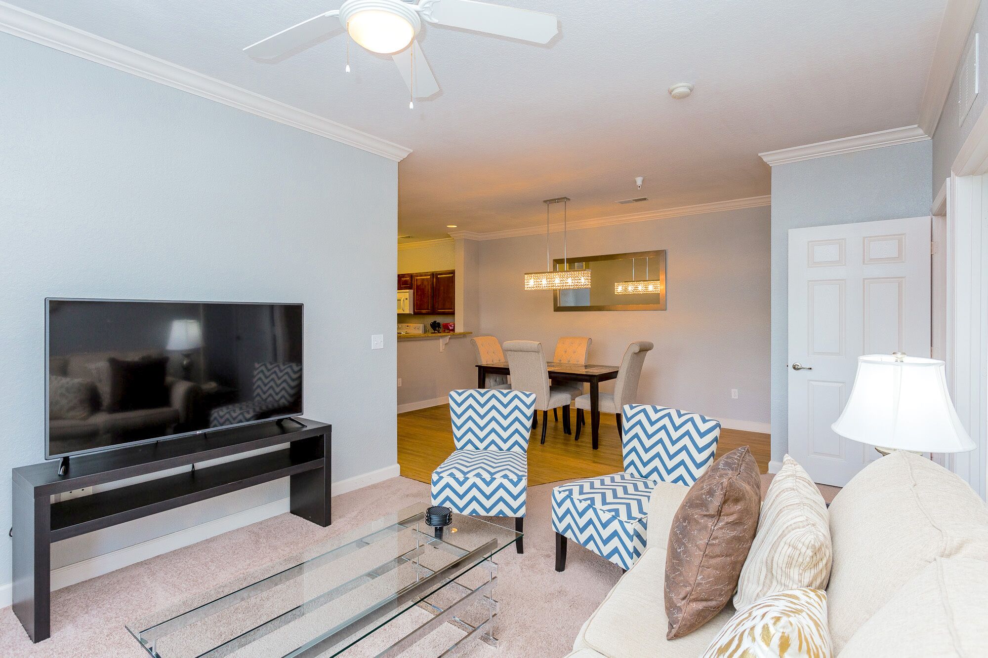 A living room with a TV, a ceiling fan, and a dining area with chairs and a table.
