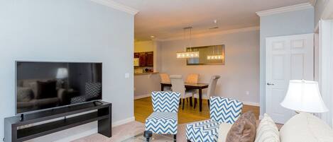 A living room with a TV, a ceiling fan, and a dining area with chairs and a table.