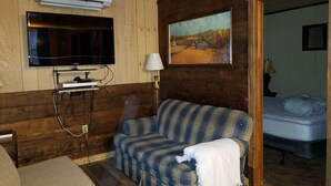 Une pièce chaleureuse avec un décor intérieur en bois, un téléviseur fixé au mur, un canapé, une lampe et un tableau.