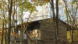 Une cabane rustique entourée d’arbres, dotée d’une terrasse en bois et d’un petit porche.
