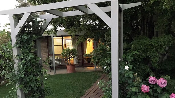 Ein Garten mit einer Pergola, einer Rasenfläche und einem Ziegelweg, der zu einem Gebäude mit großen Fenstern führt.