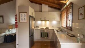 Eine kleine Küche mit Holzbalken, einem Kühlschrank, Backofen, Spüle und einem Fenster mit Jalousien.