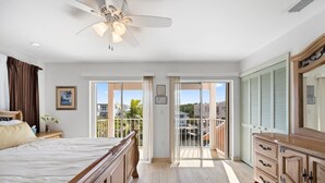 Un dormitorio con cama, cómoda, ventilador de techo y balcón con vistas al exterior.