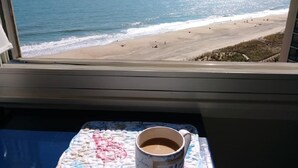 A window view of a beach with a cup of coffee on a table.