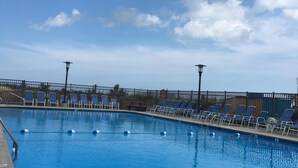 A swimming pool with blue water, surrounded by lounge chairs and a fence.