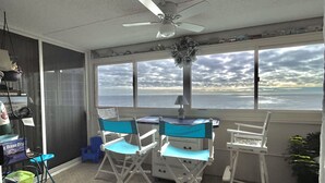 A room with a view of the ocean, a ceiling fan, and folding chairs.