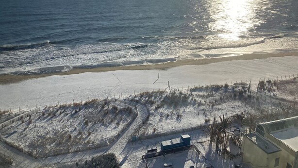 A coastal view with a beach, a fenced area, and a building with a flat roof.