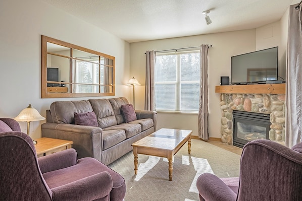 A living room with a sofa, armchairs, a coffee table, a TV, a fireplace, and a large mirror.