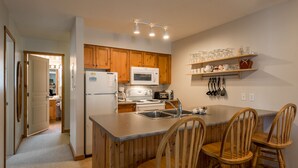 A kitchen with wooden cabinets, a refrigerator, a microwave, a sink, and a breakfast bar with chairs. -  Large Corner Quiet Top Floor Condo with A/C, BBQ, pet friendly! (Silver Star Mountain)