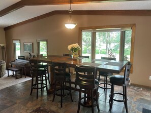 A dining area with a large table, multiple chairs, a piano, and a large window with a view of greenery. - Country Living at it’s Best (Bismarck)