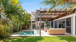 A modern outdoor pool area with a pergola, lounge seating, and lush tropical plants. - Elanda St - Luxurious Beachside Living (SUNSHINE BEACH)