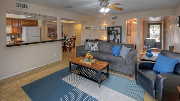 A living room with a sofa, coffee table, and a dining area with a refrigerator and wooden cabinets.