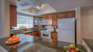 A modern kitchen with granite countertops, wooden cabinets, a stainless steel refrigerator, a microwave, and a stove.