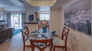 A dining area with a glass table, wooden chairs, and a cityscape painting on the wall.