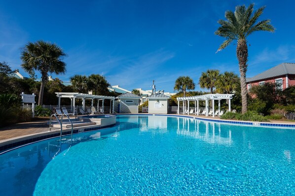 A clear blue swimming pool with lounge chairs and palm trees.