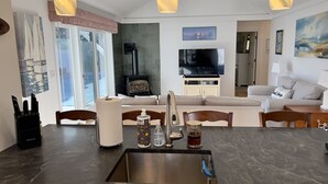 Una cuina moderna amb una illa central, fogó integrat i zona de menjador amb sofà i cadirees.
