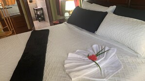 Ein ordentlich bezogenes Bett mit weißer Bettdecke, schwarzer Tagesdecke und einem Handtuch, das in Form eines Fächers mit einer roten Blume drapiert ist.
