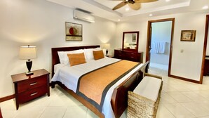 Habitación de hotel con cama, mesitas de noche, ventilador de techo, espejo y puerta que da al baño.