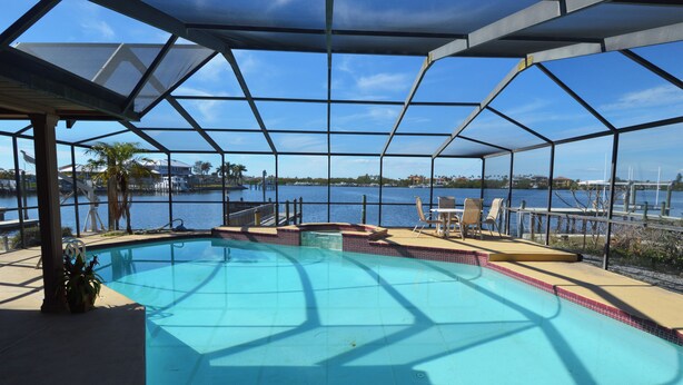 A covered swimming pool with a view of the water and distant buildings. - Home on the water w/ pool and dock (Apollo Beach)