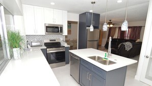 A modern kitchen with white and gray cabinets, stainless steel appliances, and a central island with a sink. - Home on the water w/ pool and dock (Apollo Beach)