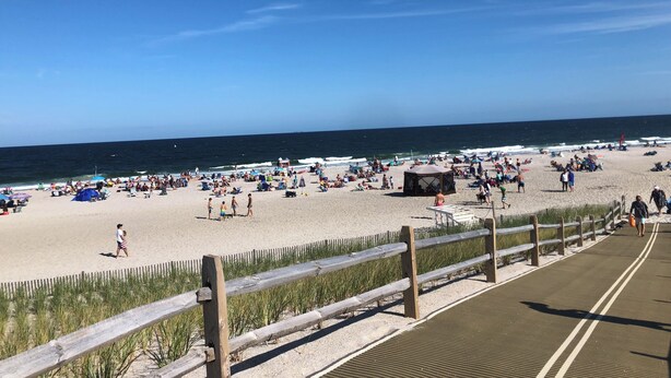 Een strand met een houten vlinderpad en een zandgebied met parasols en mensen.