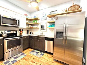 A modern kitchen with stainless steel appliances, wooden flooring, and a variety of kitchenware on shelves.