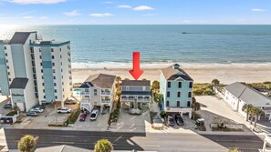 A beachfront property with a two-story building, a parking lot, and a view of the ocean.