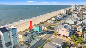 A coastal residential area with a beach, a road, and various buildings including a hotel with multiple floors and balconies.