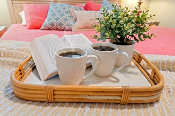 A tray with a book, two cups of coffee, and a small potted plant on a bed.